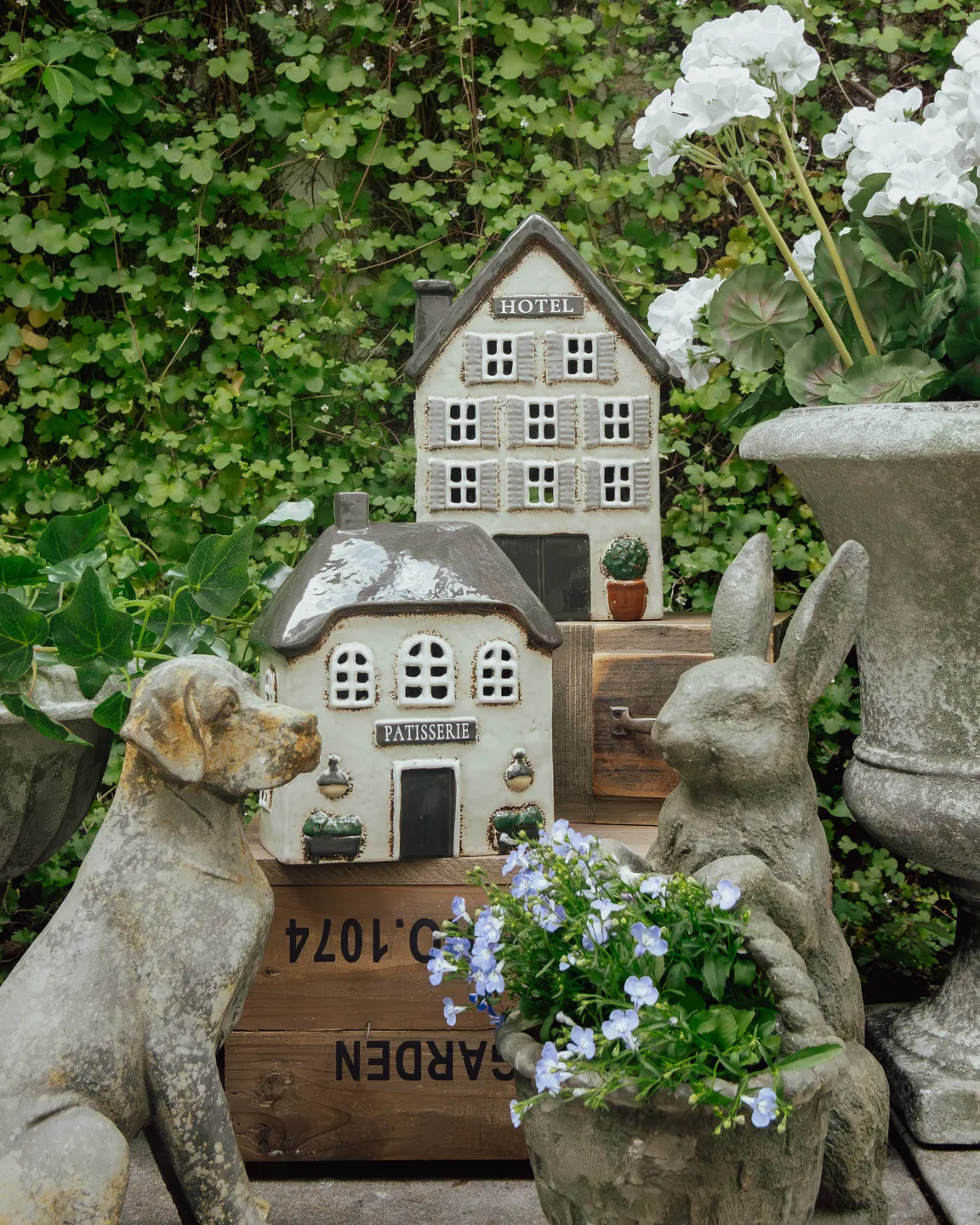 Decorative miniature house with 'Patisserie' and 'Hotel' signs, surrounded by garden elements.